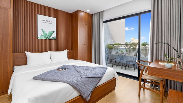 Ein modernes Hotelzimmer mit einem großen Bett, Holzwandverkleidung, Blick auf die Stadt durch große Fenster und einer kleinen Essecke mit Tisch und Stühlen.