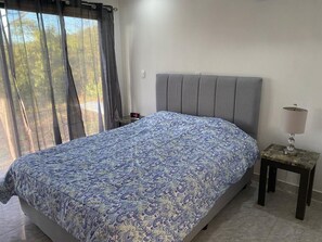 A bedroom with a bed, a nightstand, a lamp, and a window with curtains.