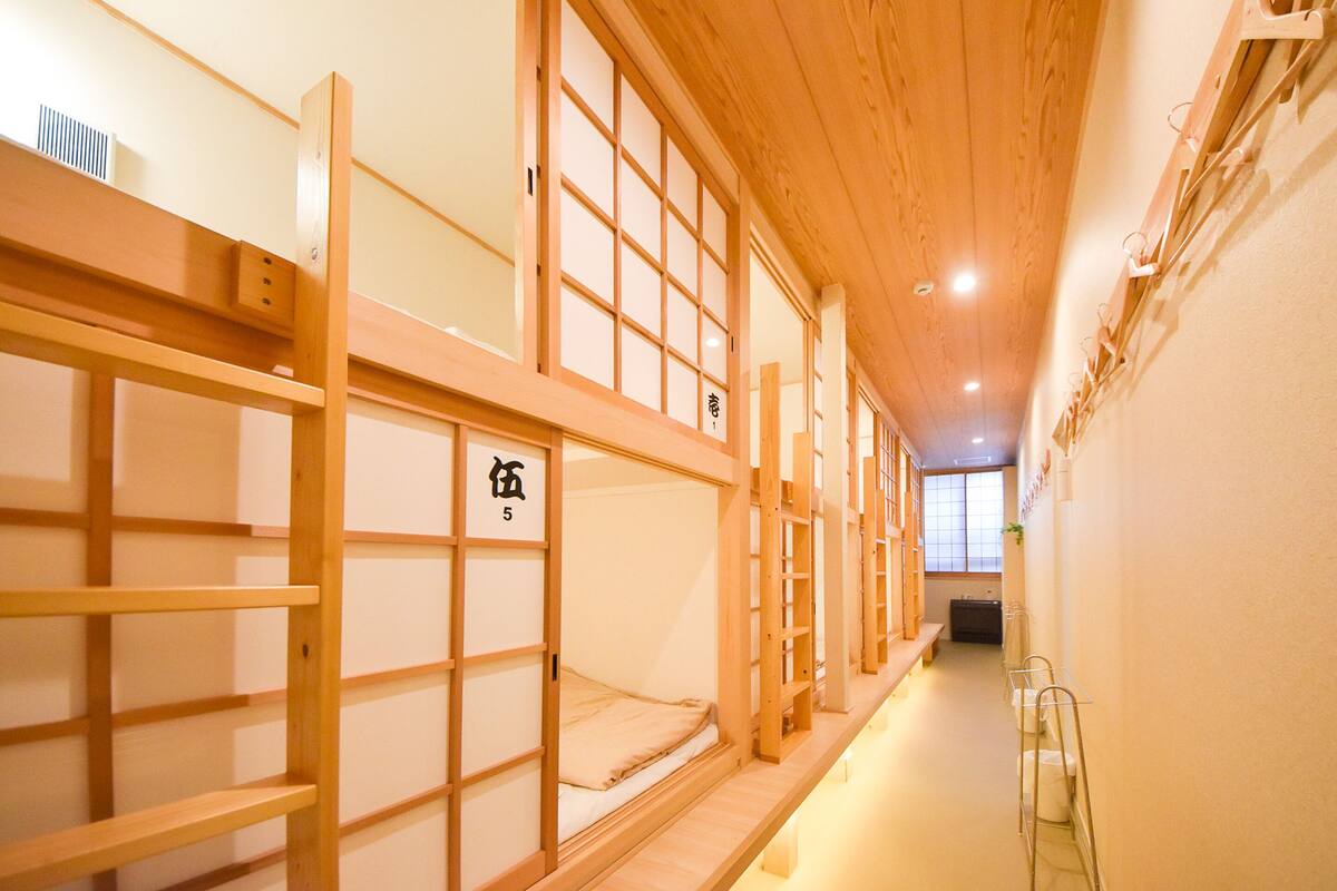 A traditional Japanese-style room with wooden bunk beds and tatami mats, a low ceiling, and a view of a traditional Japanese garden.