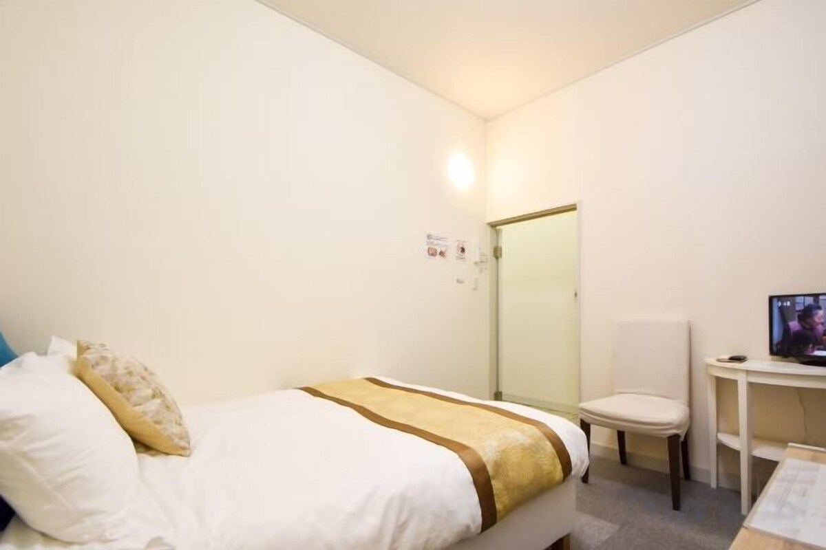 A hotel room with a bed, a chair, a desk, and a television.