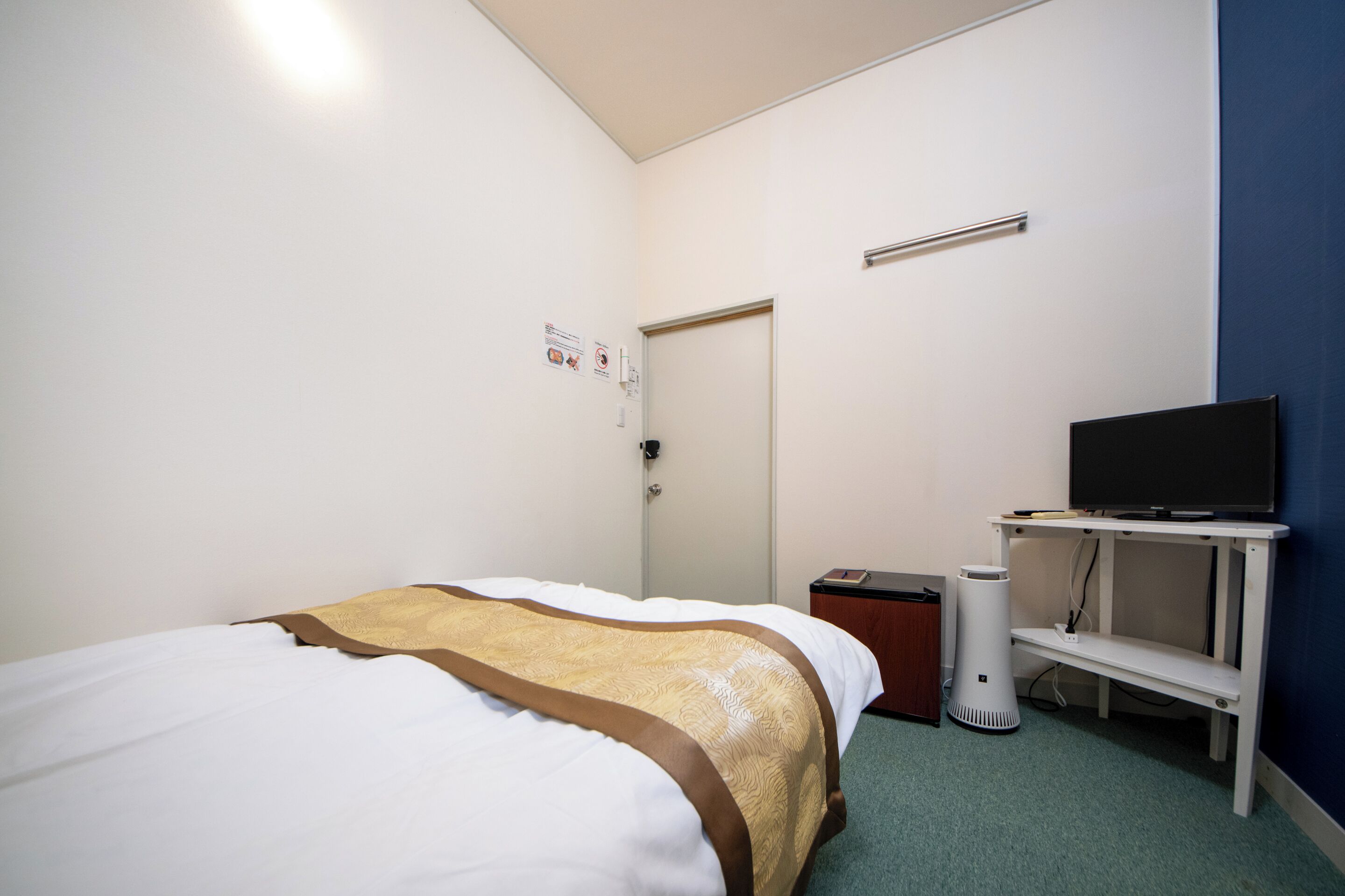 A hotel room with a bed, a television on a stand, a desk, and a door.