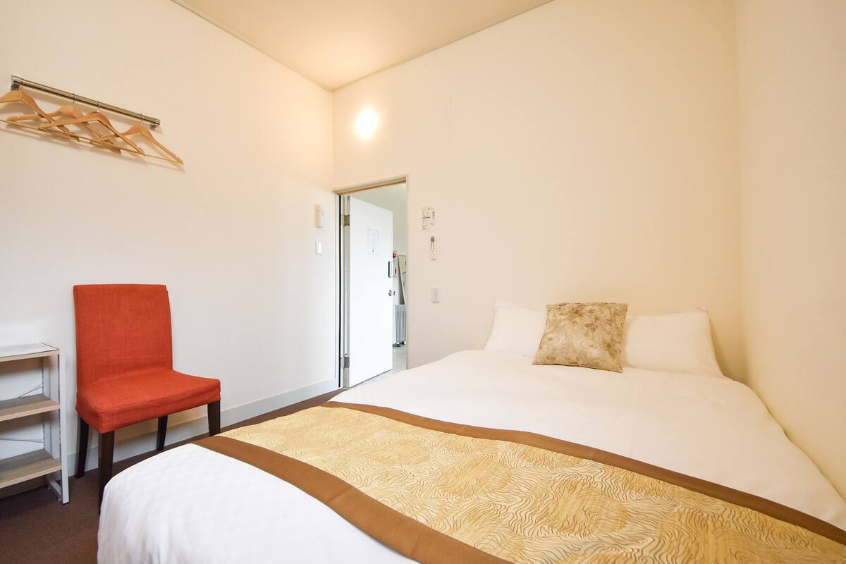 A hotel room with a bed, a chair, a desk, and a door leading to a bathroom.