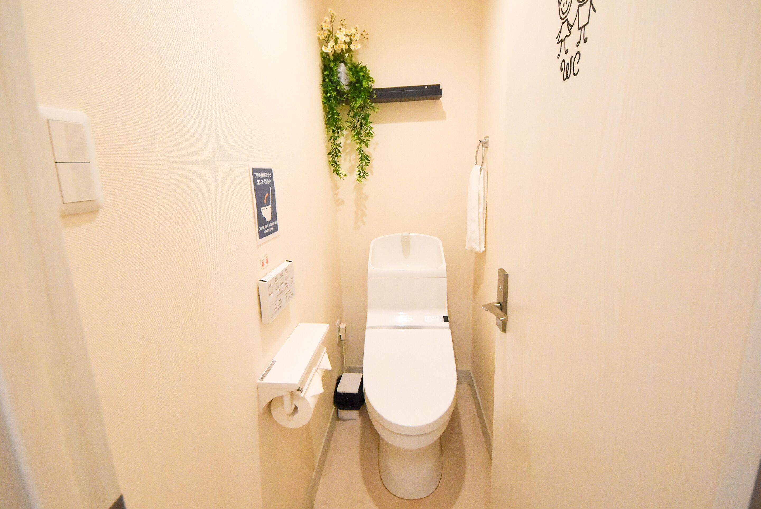 A small, clean bathroom with a toilet, a toilet paper holder, and a small shelf with a plant.