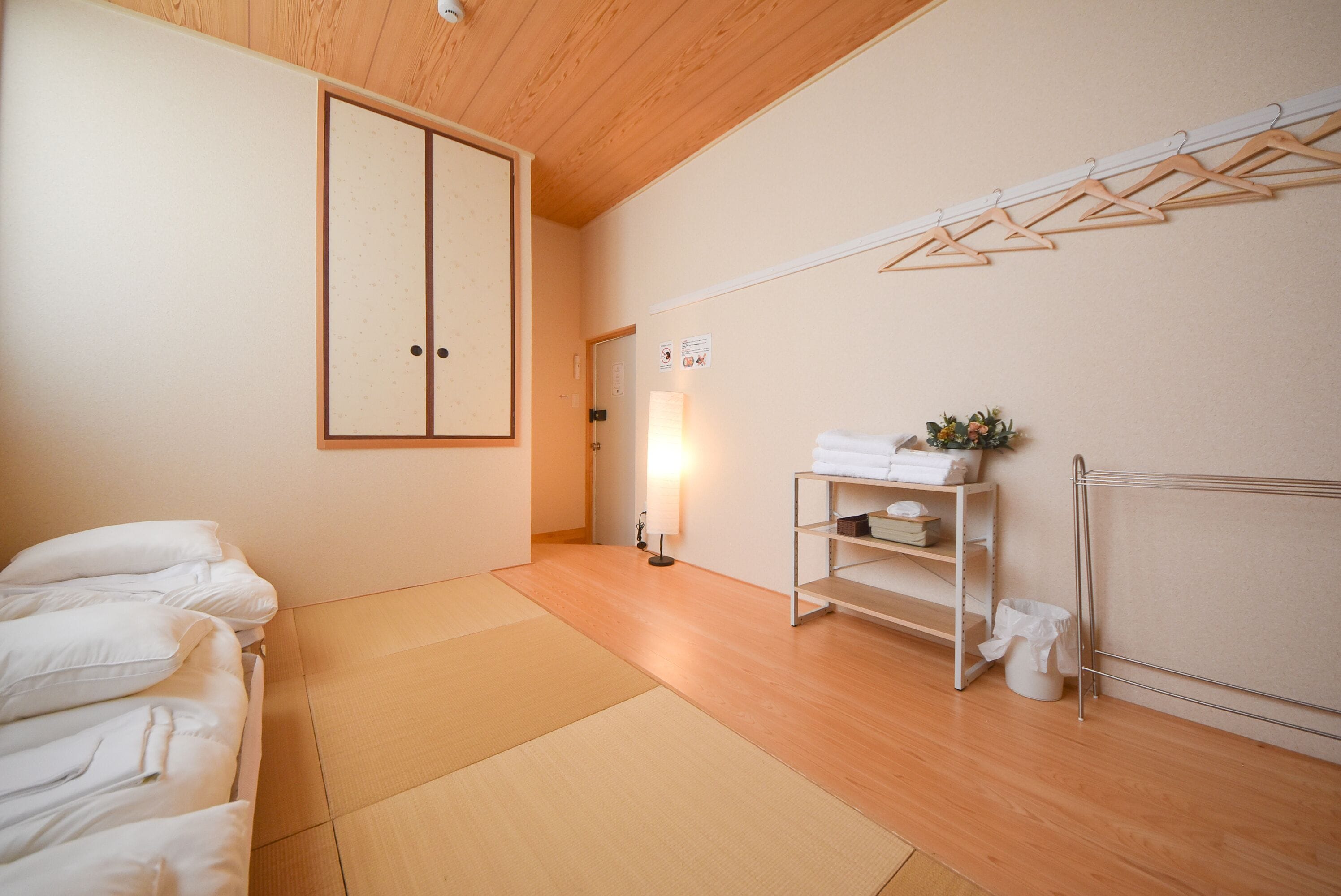 Una habitación con esteras de tatami, una cama con ropa blanca, un armario, una estantería con toallas y un radiador.
