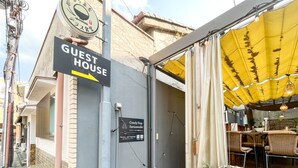 Una casa de huéspedes con un letrero que indica su ubicación, un pequeño espacio al aire libre con sillas y una mesa, y una planta en maceta.