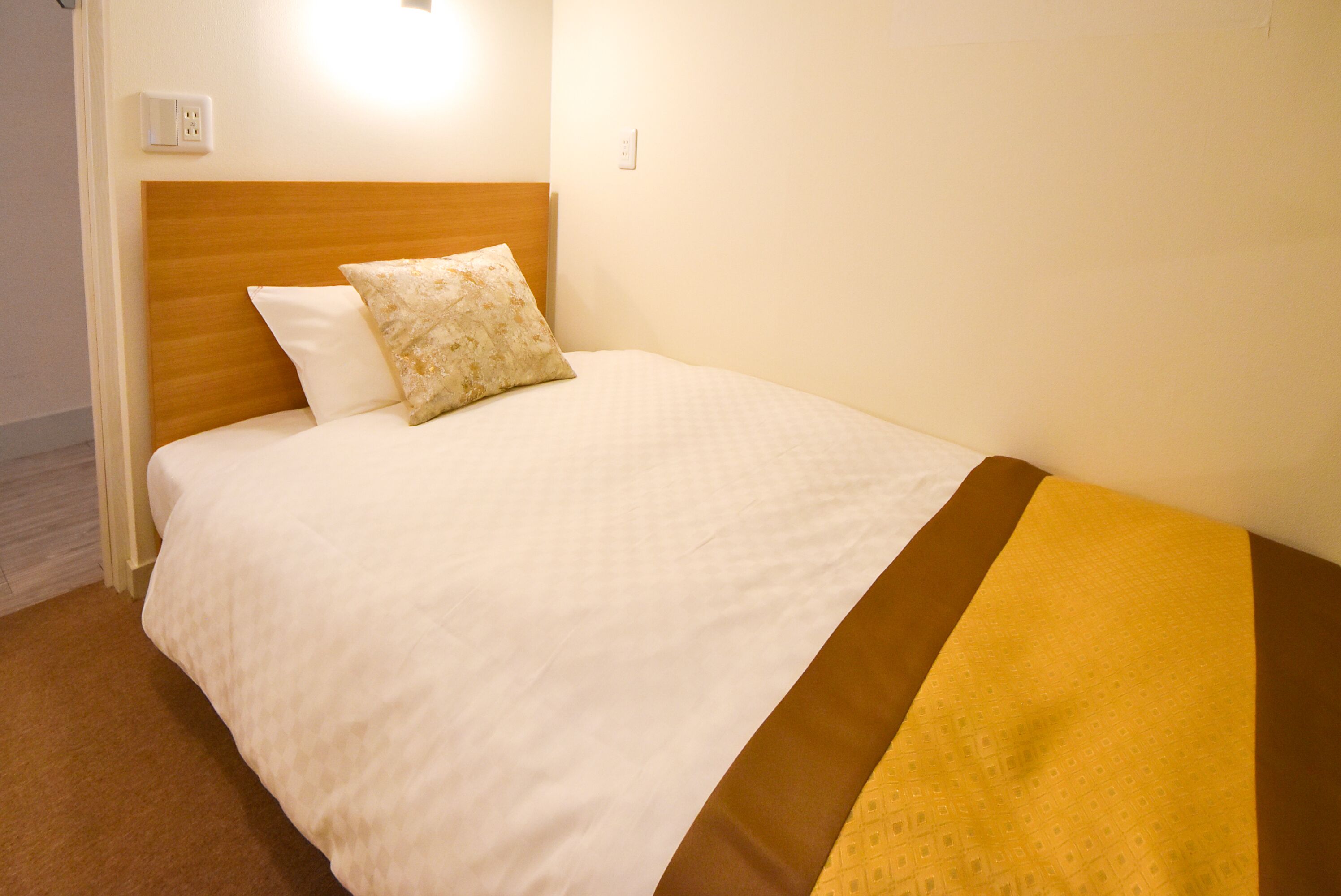 A neatly made bed with a wooden headboard, white bedding, and a brown accent.