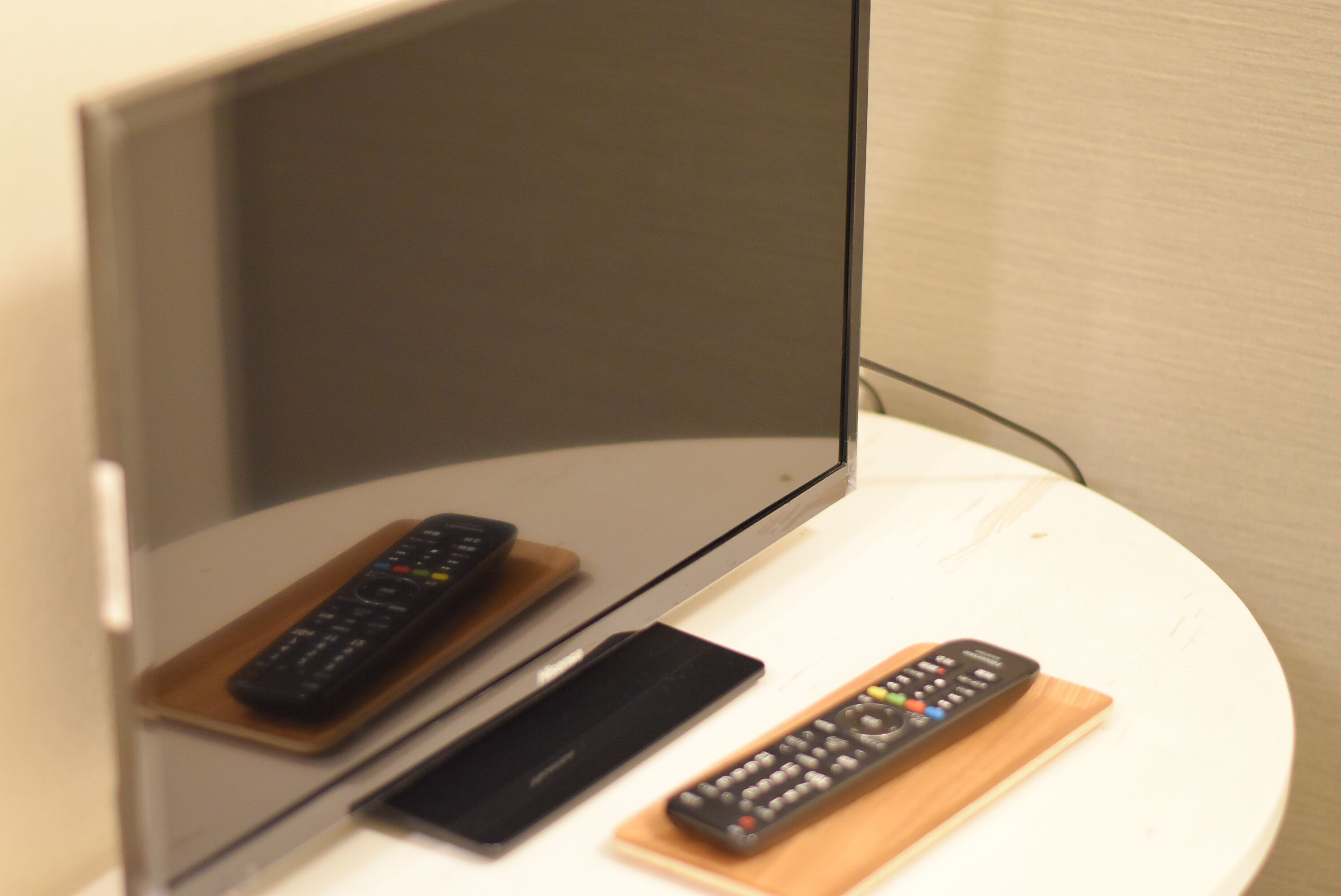 A television on a stand with two remote controls on a white table.