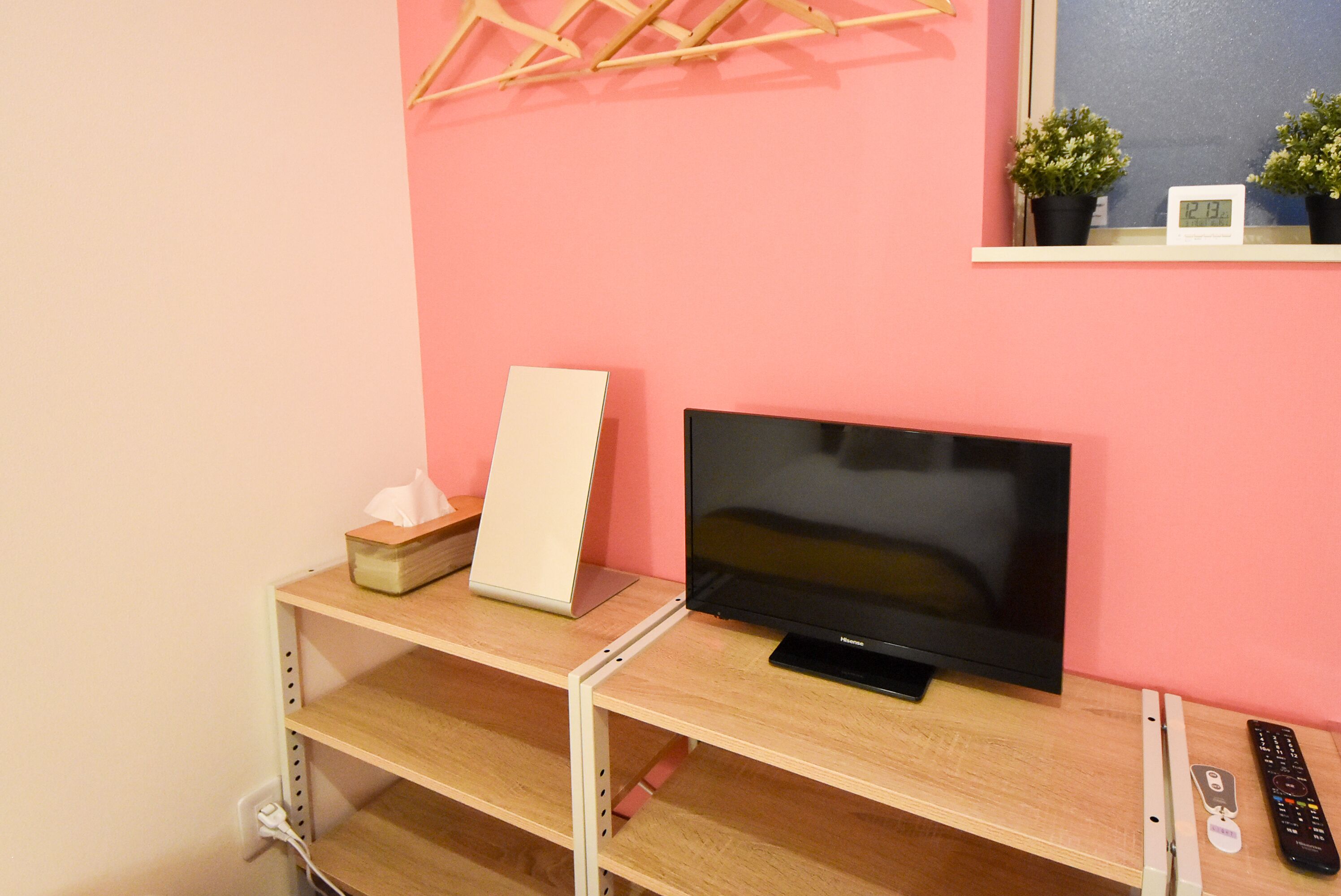 Un televisor sobre un soporte de madera, con un control remoto, una caja de pañuelos y un reloj en una estantería.