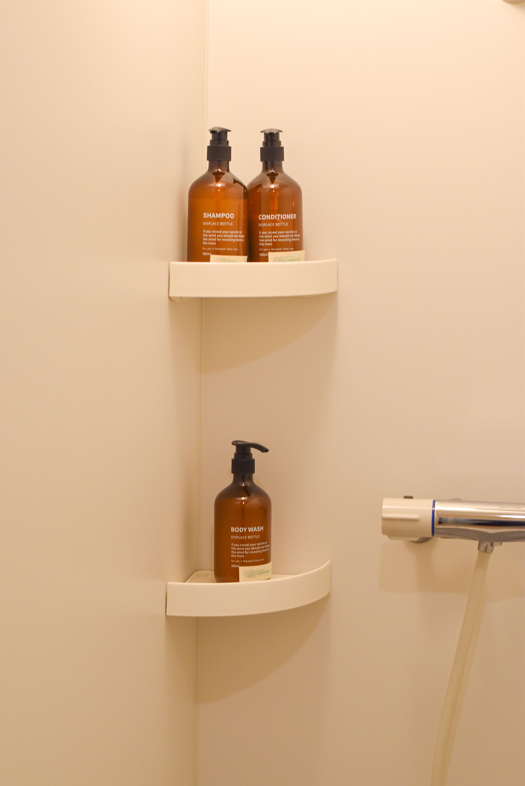 A bathroom with two shelves holding shampoo and conditioner bottles, and a body wash bottle on the lower shelf.