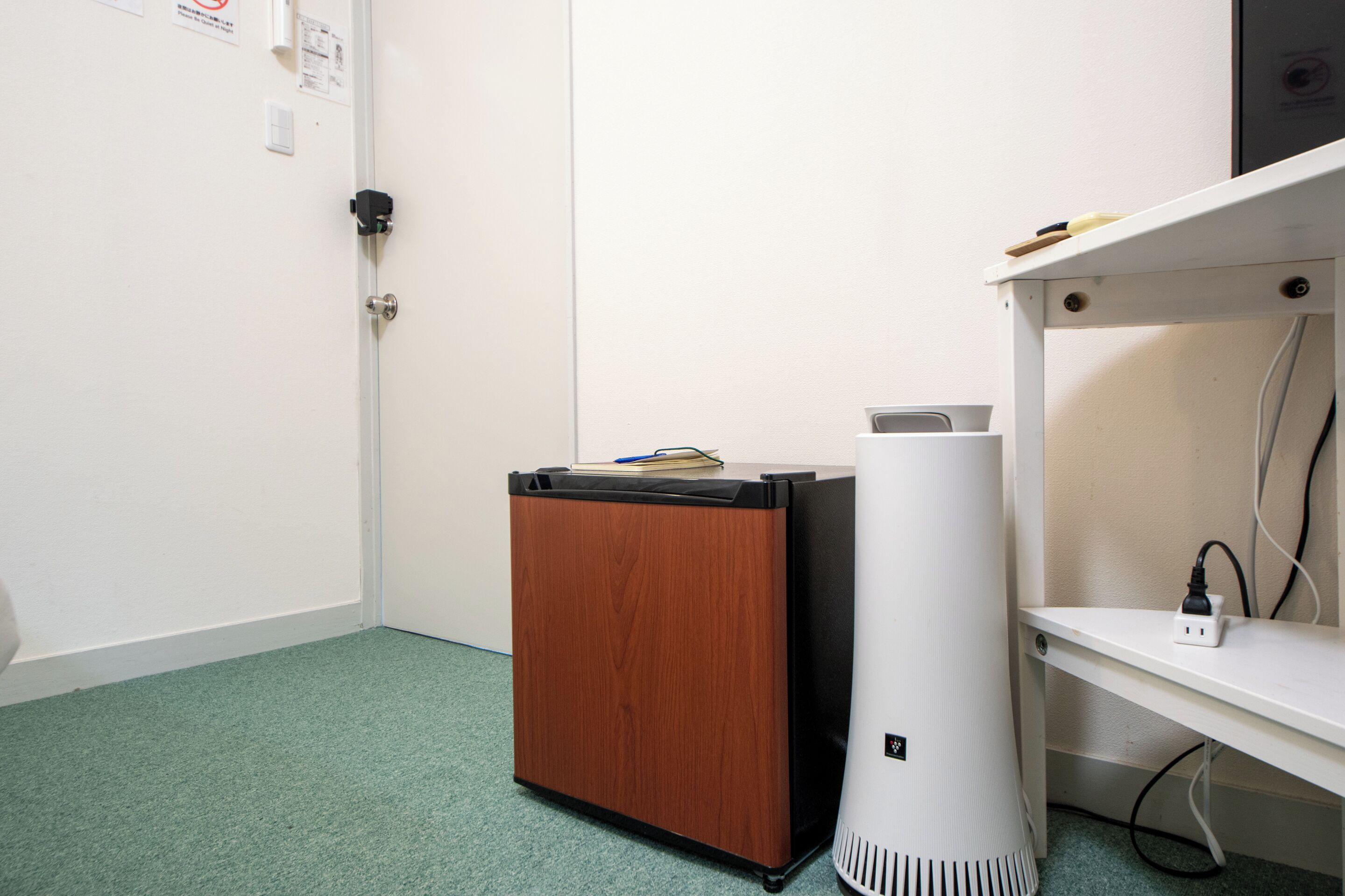 A small wooden cabinet with a black top, a white cylindrical object next to it, and a white shelf with a power outlet.