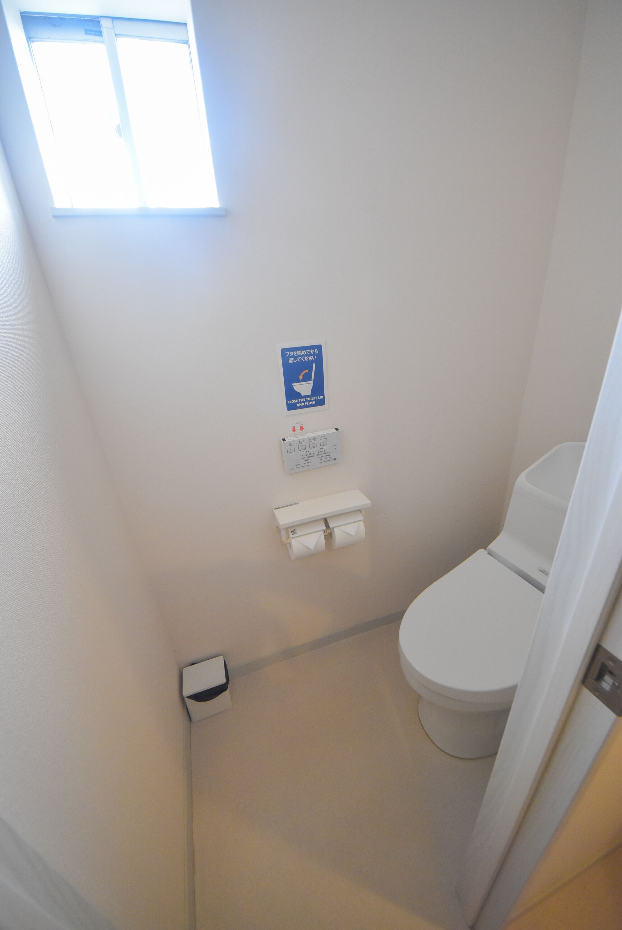A small, narrow bathroom with a toilet, a hand dryer, and a window.