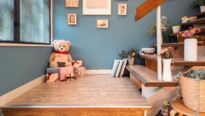 Una habitación acogedora con suelo de madera, un ventanal amplio, un osito de peluche, cuadros enmarcados en la pared y una estantería.