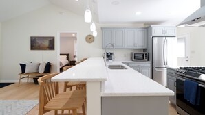 A modern kitchen with a central island, stainless steel appliances, and a dining area with wooden chairs. - Charming home near PSU - built for memorable game days and family visits (State College)