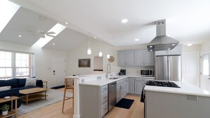 A modern kitchen with a central island, stainless steel appliances, and a dining area with a sofa and coffee table. - Charming home near PSU - built for memorable game days and family visits (State College)
