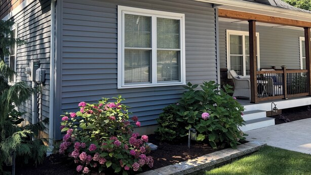 A residential house with a grey siding exterior, a brown roof, and a front porch with a wooden railing. - Charming home near PSU - built for memorable game days and family visits (State College)
