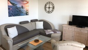 Een woonkamer met een bank, een glazen salontafel, een televisie en een klok aan de muur.