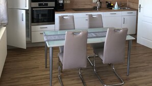 Een moderne keuken met witte kasten, roestvrijstalen apparatuur, een glazen eettafel met stoelen en een hanglamp.