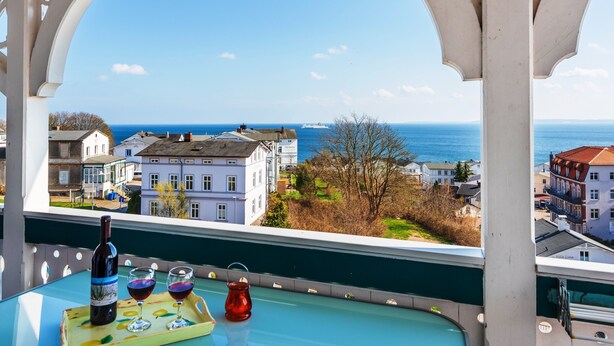 Een balkon met uitzicht op zee, een fles wijn en twee glazen op een dienblad.