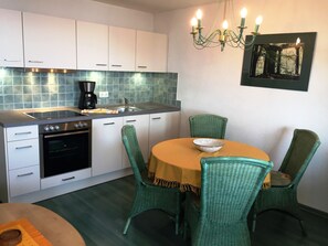 Une cuisine avec des meubles blancs, une cuisinière, un four, un évier et un coin repas avec des chaises vertes et une table ronde.