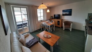 A living room with a sofa, a dining table, a TV, and a kitchen area.