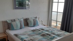 A bedroom with a bed, pillows, a nightstand, a lamp, a window, and a view of the outside.
