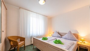 Et soveværelse med seng, stol, natbord, lampe og et vindue med gardiner.