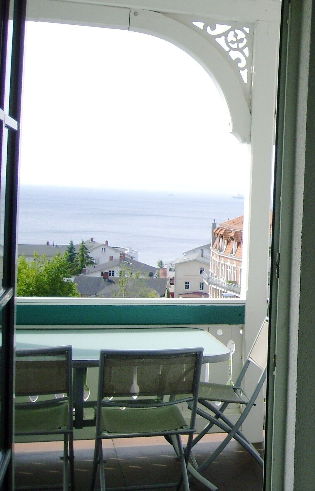 A balcony with a table and chairs, overlooking a coastal view with buildings and the sea.