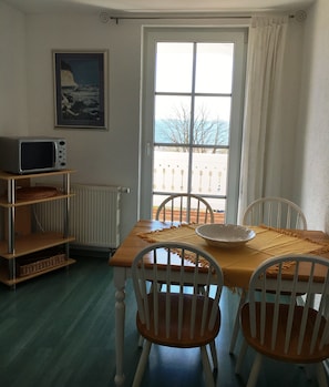 A dining area with a table, chairs, a bowl, a framed picture, a shelf, and a window with a view.