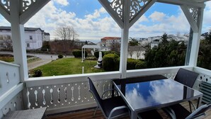 A covered outdoor area with a table and chairs, a view of a residential area, and a clear sky.