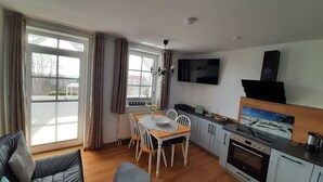 A compact living space with a dining area, kitchenette, and a TV mounted on the wall.