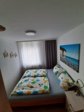 A bedroom with a bed, a window with curtains, a wall-mounted picture, and a bedside table.