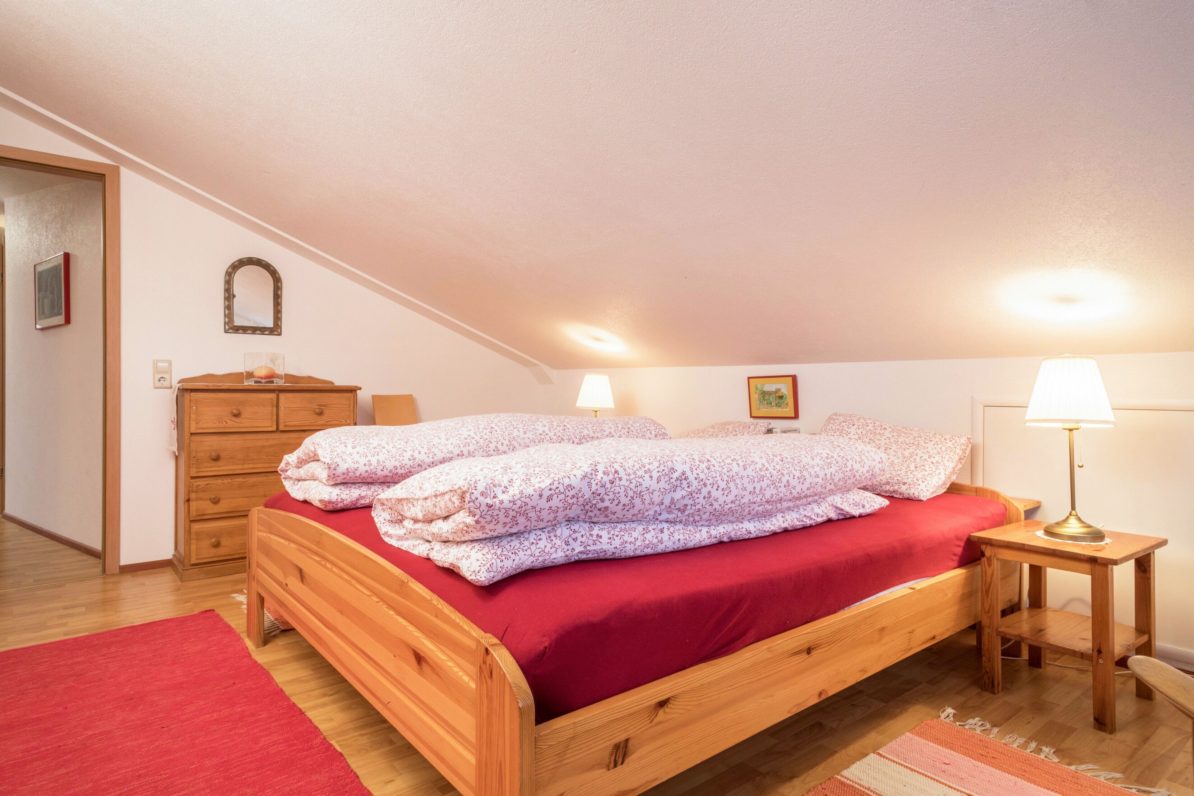 Un dormitorio con una cama de madera, dos lámparas de noche, un tapete rojo y un aparador de madera.