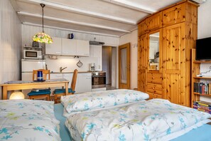 A compact bedroom with two beds, a wooden wardrobe, a kitchenette, and a television.