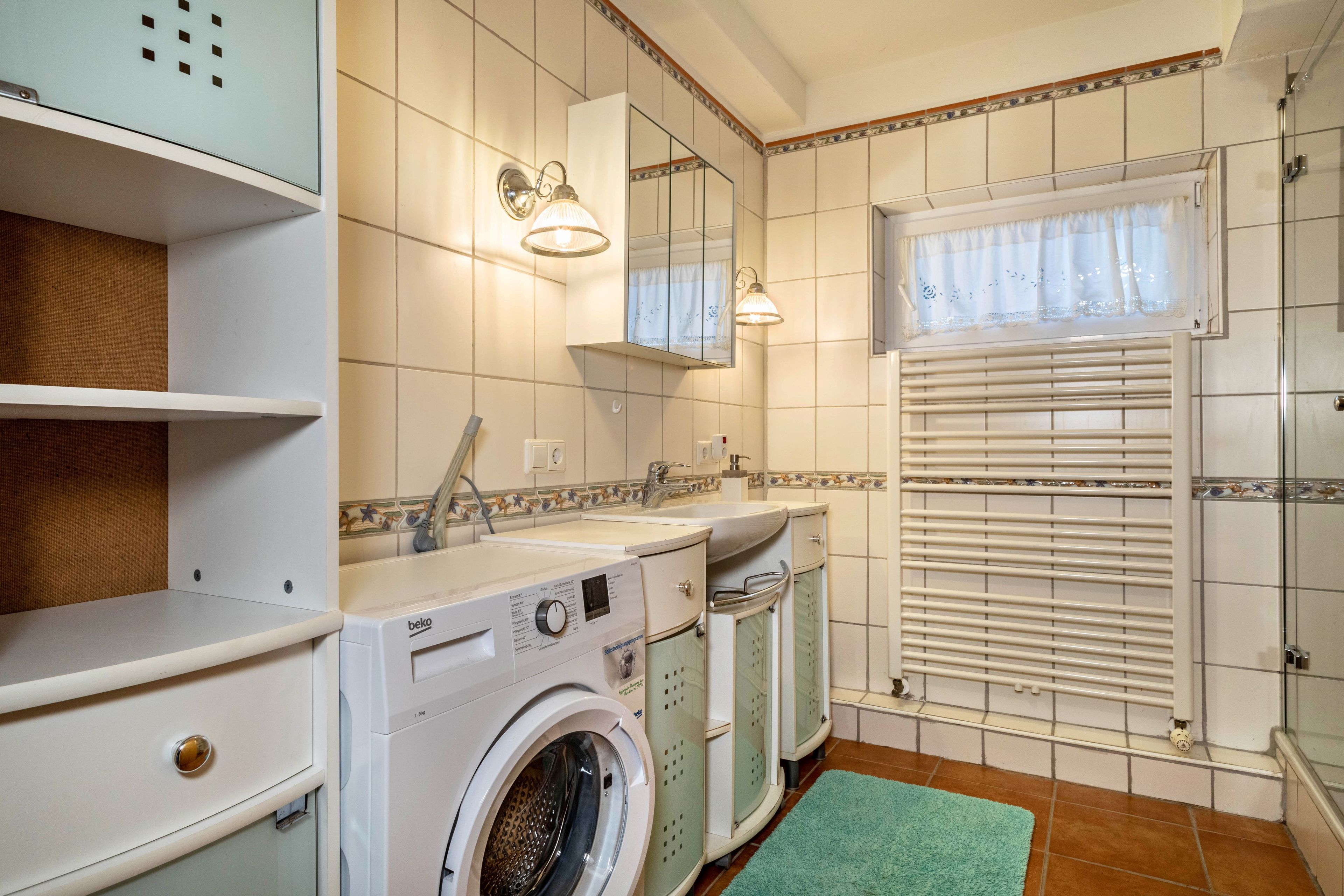 Ein kleines Badezimmer mit Waschmaschine, Spüle und Spiegel.