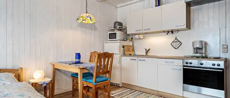 Cocina compacta con alacenas blancas, una mesa de comedor de madera, una silla, una lámpara colgante y un horno empotrado.