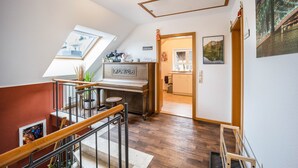 A room with a piano, a skylight, a wooden staircase, and a cityscape painting. - Holiday Apartment in the Countryside with Mountain View, Balcony and Wi-Fi (Wolpertswende)