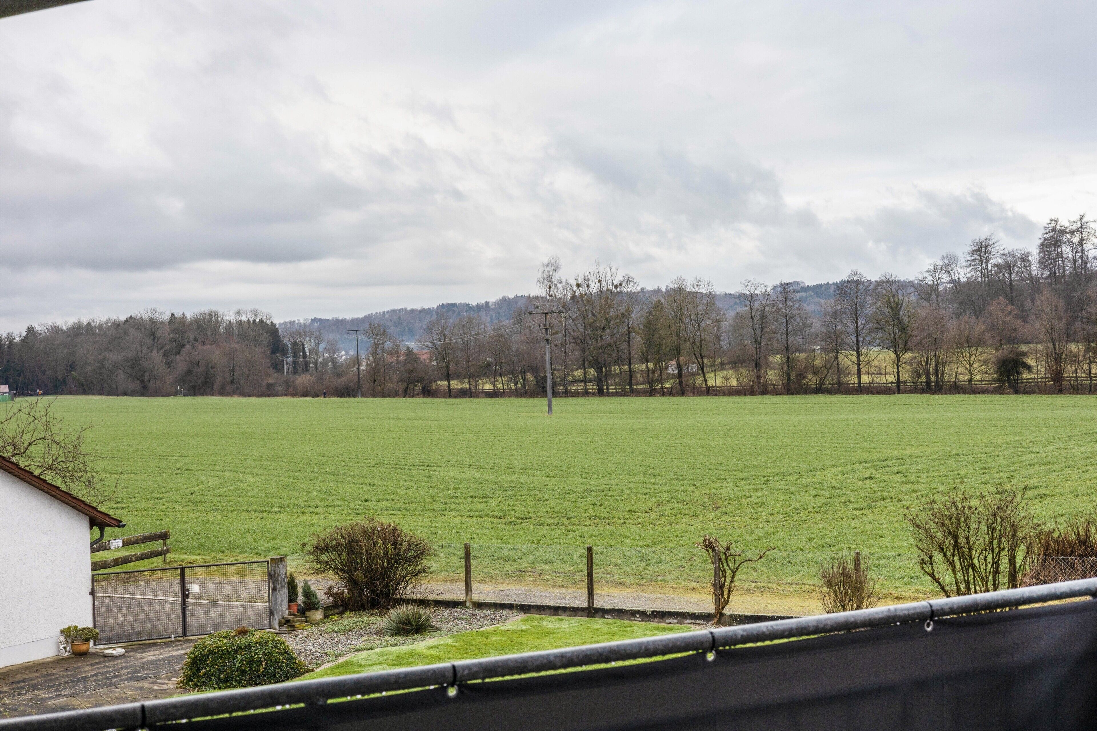 Uitzicht op een groen veld vanaf een gebouw, met een omheind gebied en een klein gebouwtje met dak.