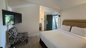 Una camera d'albergo con un letto, una sedia, una TV a muro e un ingresso che porta al bagno.