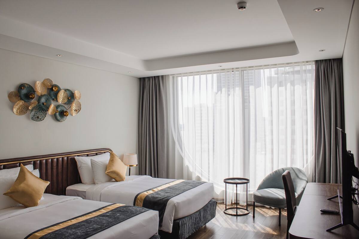 Une chambre d’hôtel avec deux lits, un bureau, une chaise, une télévision et une grande fenêtre avec des rideaux.