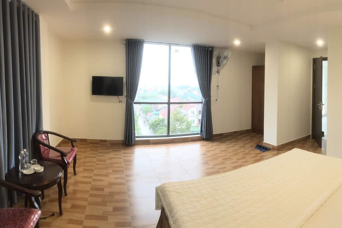 Une chambre d’hôtel comprenant un lit, un bureau avec une chaise, un téléviseur fixé au mur et une grande fenêtre avec des rideaux.