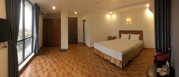 A hotel room with a large bed, a wooden floor, a window with curtains, a bedside table, and a chair.