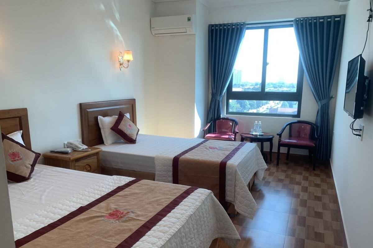 Une chambre d’hôtel avec deux lits, une petite table, une chaise et une fenêtre avec des rideaux.