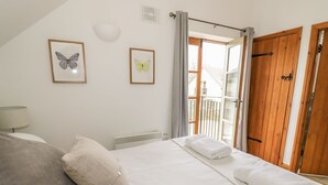 A bedroom with a bed, pillows, a radiator, a window with curtains, and two framed butterfly pictures on the wall. - Bridge House (Cirencester)