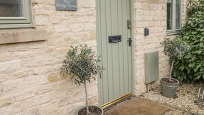 A stone building with a green door, a sign reading "36 The Bridge House," and a small potted plant beside the door. - Bridge House (Cirencester)