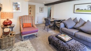 A cozy living room with a patterned armchair, a grey sofa, a coffee table with magazines, and a dining area with a table and chairs. - Violet Cottage (Ambleside)
