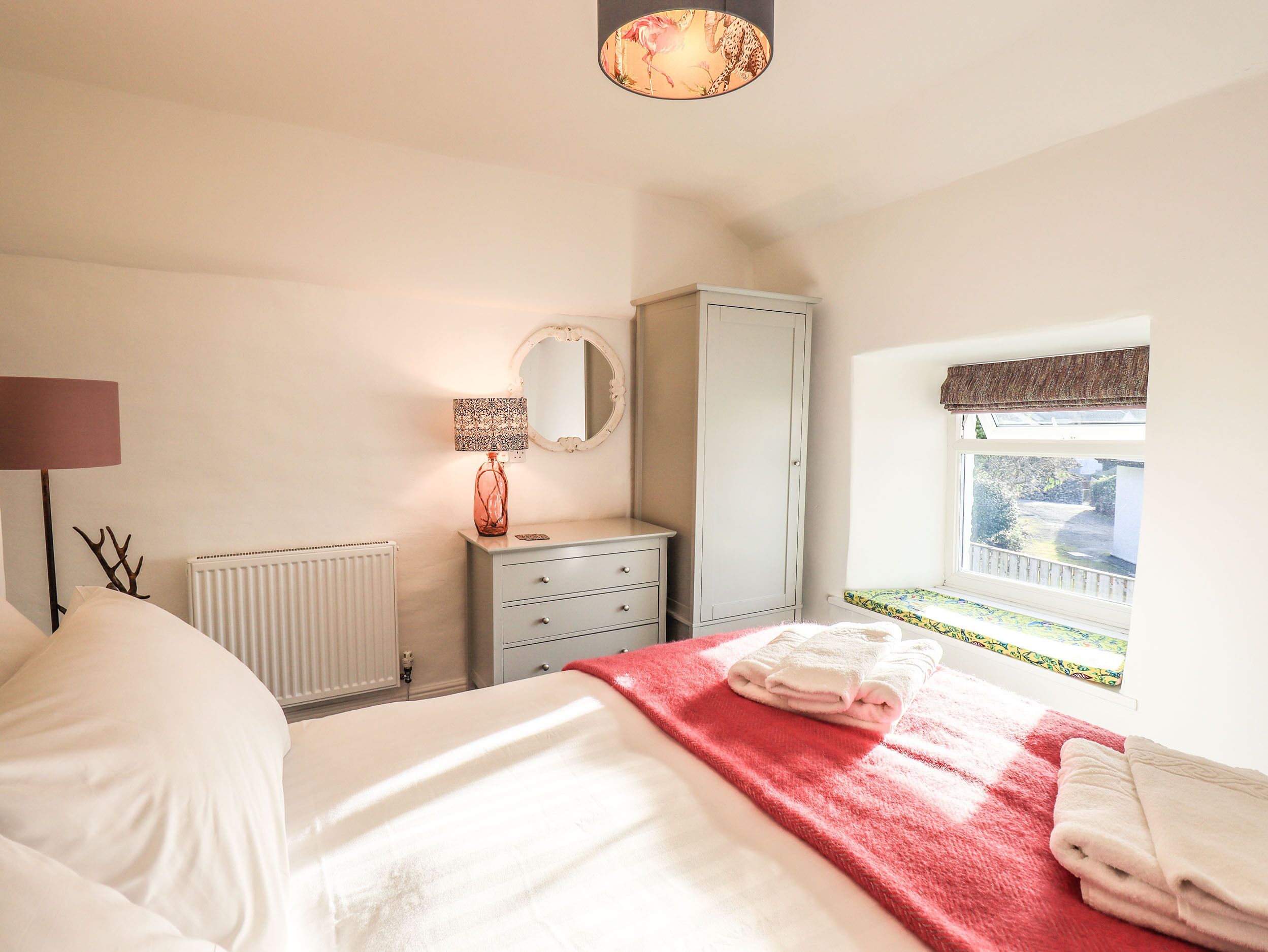 A bedroom with a bed, a dresser, a mirror, a lamp, and a window with a view.