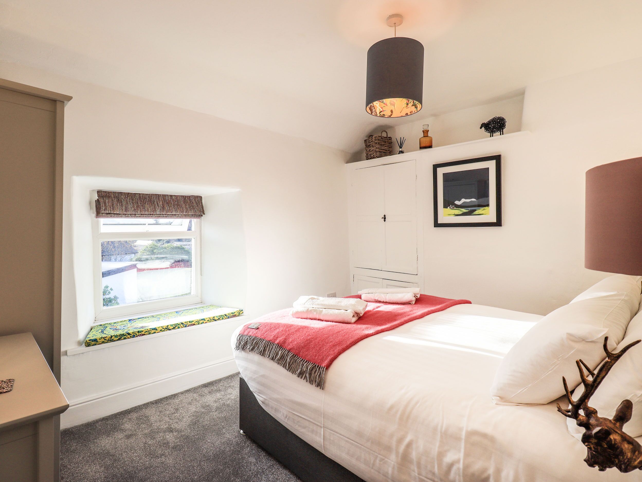 A bedroom with a bed, a bedside table, a window with a view, a wardrobe, and a hanging light fixture.