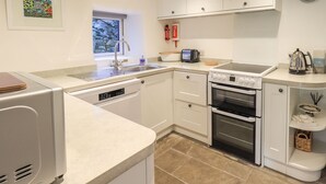 A modern kitchen with white cabinets, a built-in dishwasher, a stove, and a sink. - Violet Cottage (Ambleside)