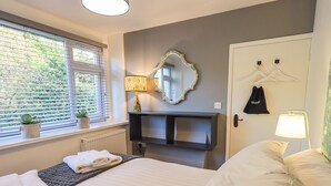 A hotel room with a bed, a bedside table, a mirror, a lamp, a radiator, and a window with blinds. - Violet Cottage (Ambleside)