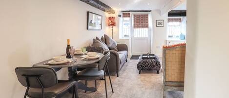 A dining area with a table set for four, a sofa, and a patterned ottoman.